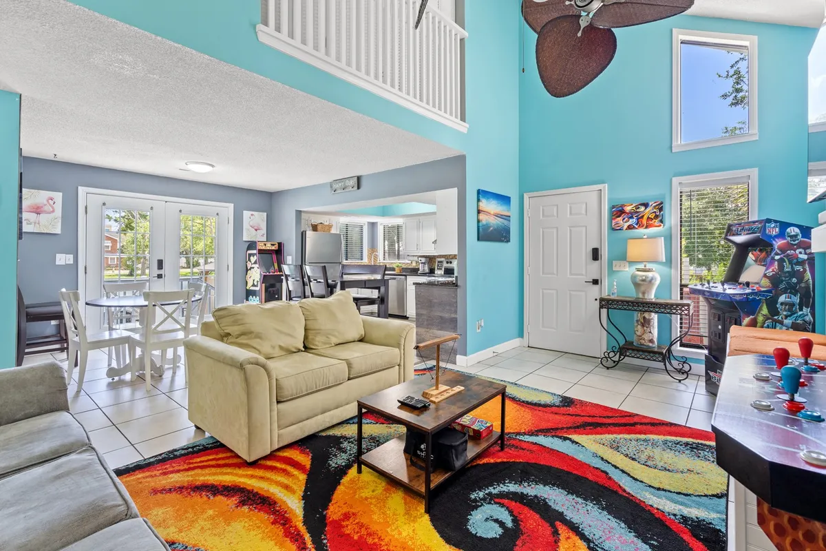 This inviting view captures a colorful rug, a plush sofa, a stand-up arcade machine, and a glimpse of the dining area. The cheerful mood and diverse furnishings highlight the space’s versatility, supporting both entertaining and quiet moments.