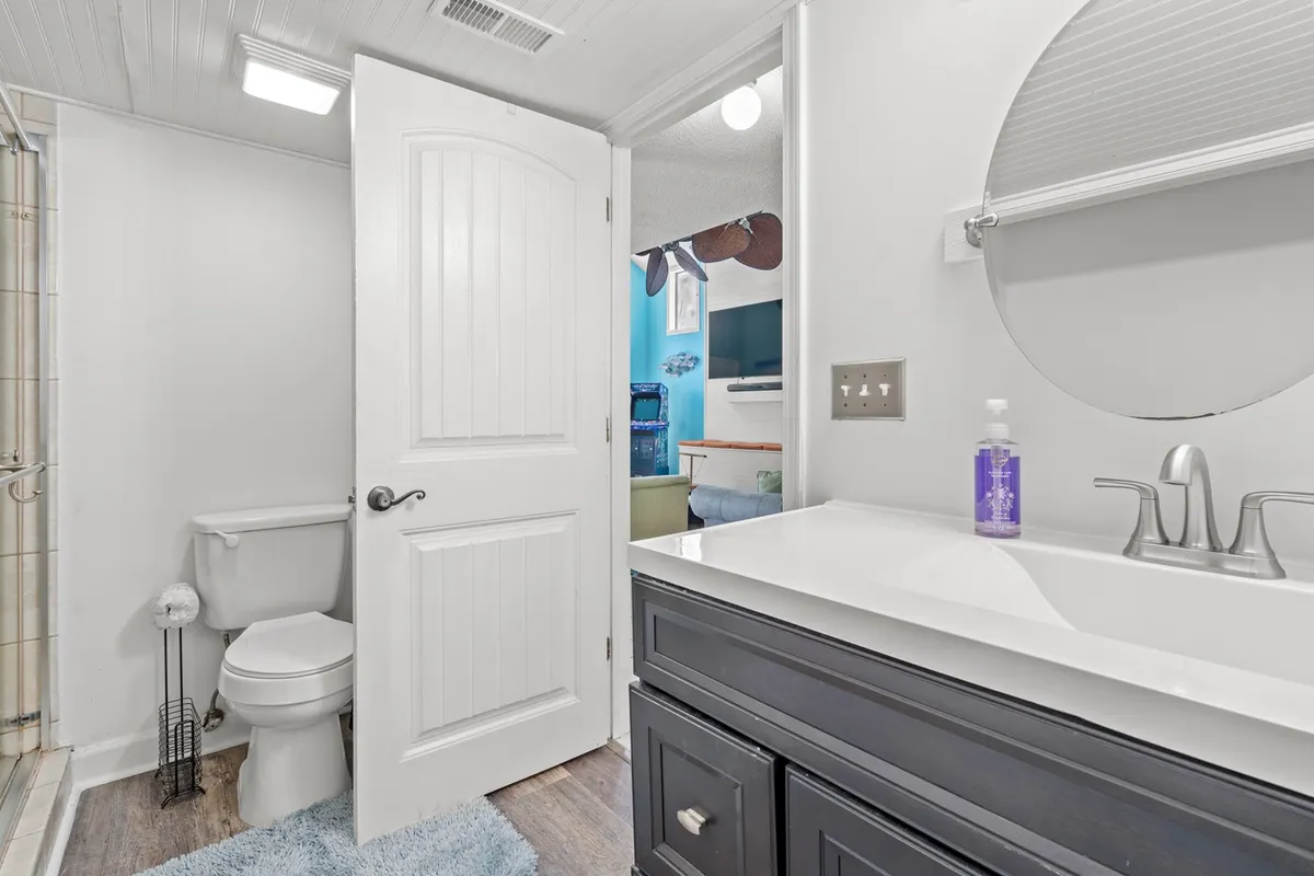 A modern bathroom with a vanity and sink, glass shower stall, toilet, and mirror. The space is bright and inviting, suggesting convenience for larger groups with multiple bathrooms available.