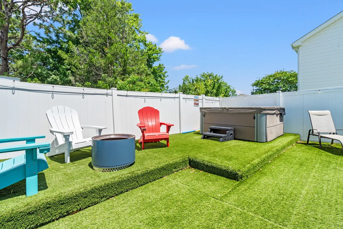 A cozy outdoor space with colorful Adirondack chairs circles a fire pit, and a bubbling hot tub is nearby. The atmosphere is vibrant yet relaxed, offering spaces for socializing, soaking, and enjoying evening gatherings.