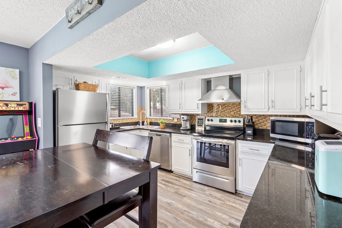 A modern, inviting kitchen and dining area with a kitchen island, stainless steel appliances, and a spacious dining table. A colorful accent wall adds personality, while the ample workspace makes it easy for several cooks to work at once. The open-plan design encourages group cooking, dining, and celebration.
