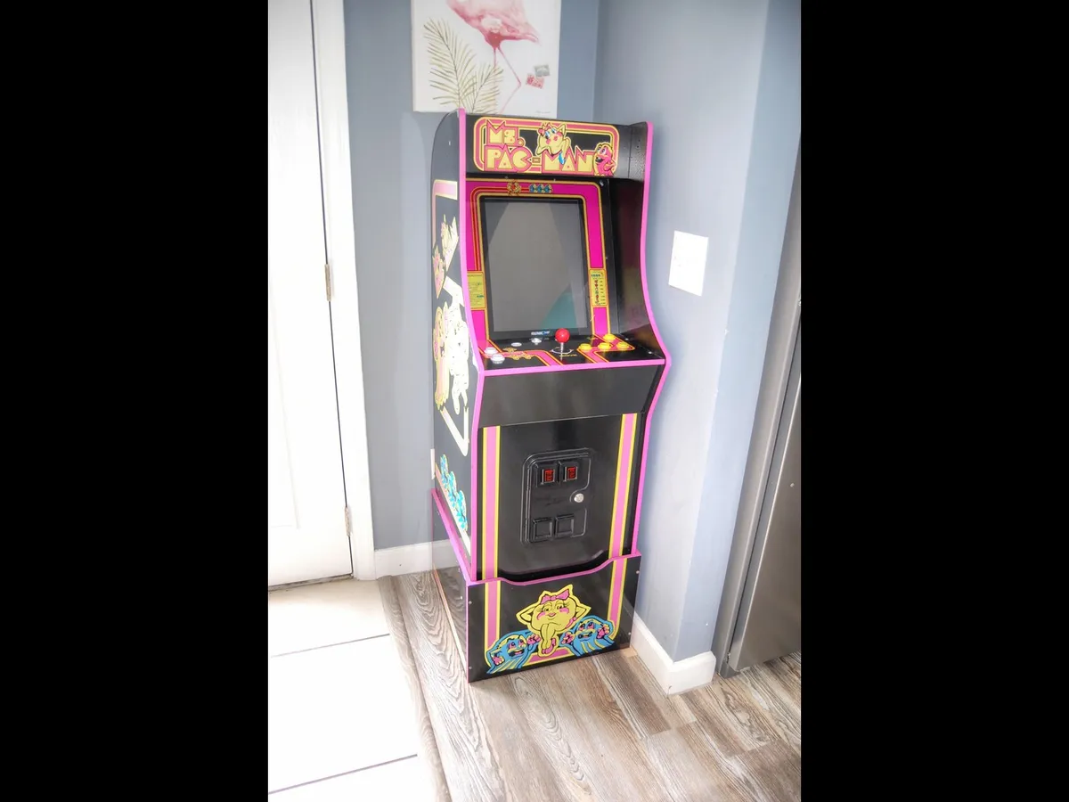 A close-up of a nostalgic Pac-Man arcade machine with colorful artwork, set on wooden flooring. The area offers a fun spot for friendly competition and shared gaming experiences.